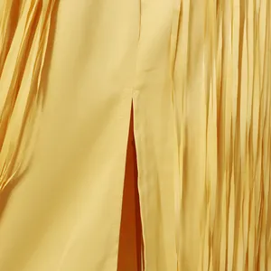 Detailed macro view showing the yellow tassel fringe and refined slit on a long dress.