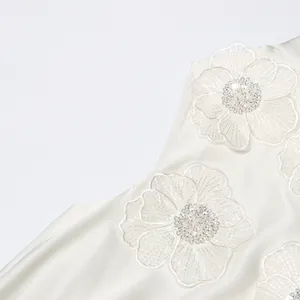 Détail rapproché montrant les applications florales 3D sur une robe blanche élégante sans manches