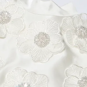 Gros plan détaillé sur les appliques florales et les perles d'une robe blanche élégante
