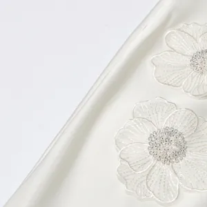 Détail d'applique florale blanche avec broderie de perles et paillettes sur tissu satiné