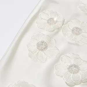 Gros plan détaillé des appliqués floraux et perles sur une robe élégante blanche