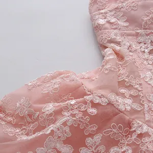 Close-up detail of delicate floral lace embroidery and sequins on pink mesh dress
