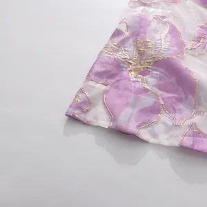 Primo piano del tessuto con stampa floreale viola e ricamo dorato per abito lungo estivo.