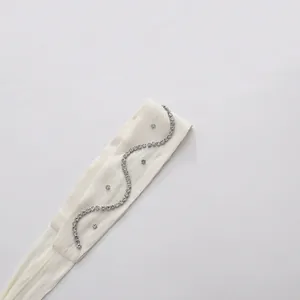 Close-up detail of an elegant white fabric belt with curved silver rhinestone embellishments