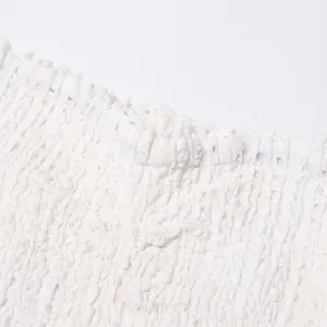 Detail shot of white smocked dress fabric featuring delicate scalloped eyelet embroidery texture
