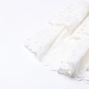 Close-up macro shot of intricate white eyelet lace embroidery on a tiered ruffle dress.