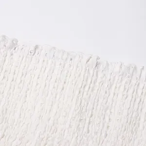 Close-up of white hollow-out crochet and smocked fabric detail on a luxury summer dress