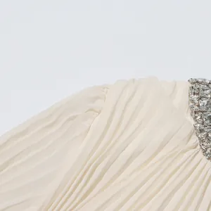 Close-up view of elegant pleated cream dress featuring shimmering rhinestone neckline details