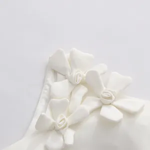 Detailed macro view of 3D fabric flower appliques on a white sleeveless dress shoulder