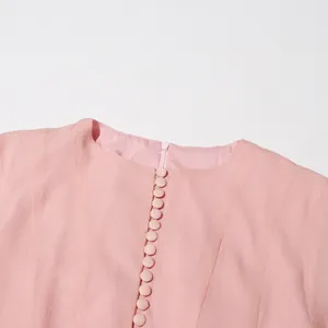 Detailopname van een elegante roze jurk met ronde hals en met stof beklede knopen
