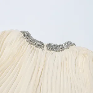 Close-up of elegant rhinestone embellished collar and pleated fabric on cream dress