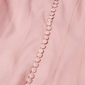 Detailopname van met stof beklede knopen op een elegante roze jurk van crêpe.