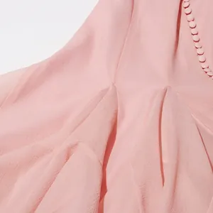 Gedetailleerde close-up van roze chiffon jurk met beklede knopen en elegante plooien