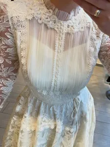 Detail of white lace dress with floral embroidery and pearl neck embellishment