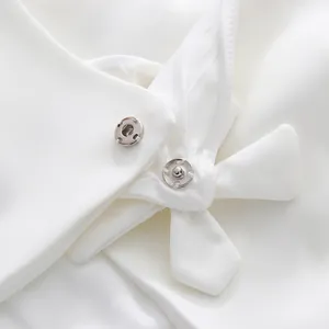 Macro view showing the metallic snap fasteners and fabric flower detail on white dress