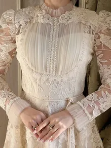 Close-up of elegant cream lace dress with intricate floral embroidery and pearl cuffs.