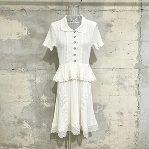 Detailed view of white knit dress with lace embroidery and ruffled waist decoration