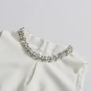 Detail shot of the rhinestone-embellished neckline on a white sleeveless dress.