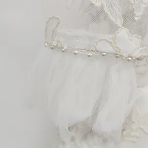 Close-up of white lace dress featuring delicate floral embroidery and pearl bead trim