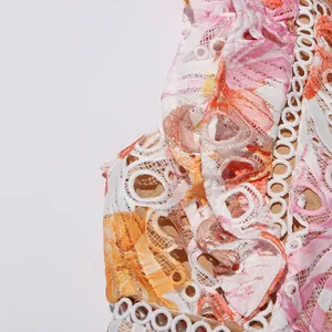 Gros plan sur le tissu en dentelle brodée aux motifs floraux roses et orange pour robe femme.