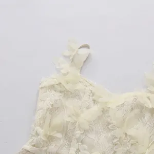 Detailed macro view of white lace dress featuring delicate 3D butterfly appliqués on straps