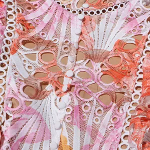 Gros plan de la broderie de dentelle rose et orange avec de délicats petits boutons blancs.