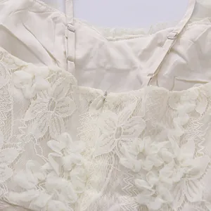 Close-up of delicate floral lace embroidery and invisible zipper on a white camisole dress.