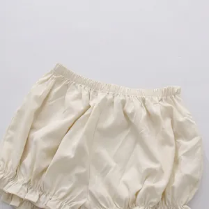 Close-up detail of cream white baby bloomers featuring elastic waistband and ruffled leg hem