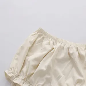 Detail view of a cream-colored solid dress with elastic waistband and soft ruffled hem