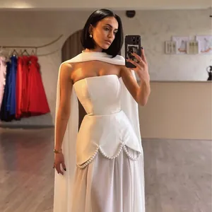 Elegant white strapless evening gown featuring intricate pearl beading and a dramatic flowing cape