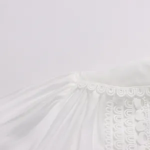 Gros plan sur les détails de broderie en dentelle d'une robe blanche de style français.