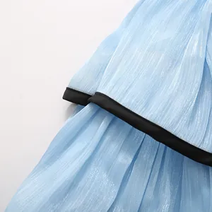 Detailed macro view of light blue shiny pleated fabric with black piping on a layered dress