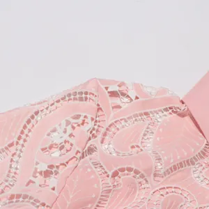 Close-up macro detail of intricate white lace embroidery on a elegant pink designer dress.