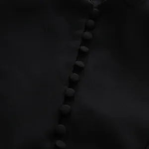 Nahaufnahme eleganter stoffbezogener Knöpfe an einem schicken schwarzen Businesskleid.