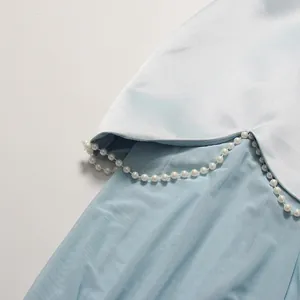 Close-up of elegant light blue satin dress with delicate pearl bead trim and mesh detail