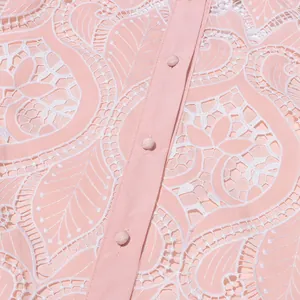 Close-up of intricate white hollow-out embroidery and pink fabric-covered buttons