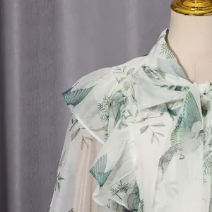 Detailaufnahme einer weißen Netzbluse mit grünem Vogeldruck und Rüschenkragen