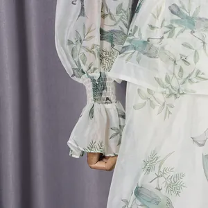 Nahaufnahme von weißen Mesh-Ärmeln mit elegantem Blumen- und Vogelprint und gesmokten Bündchen