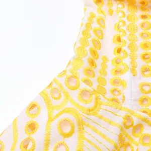 Gros plan sur la broderie anglaise jaune complexe d'un tissu de robe d'été blanc