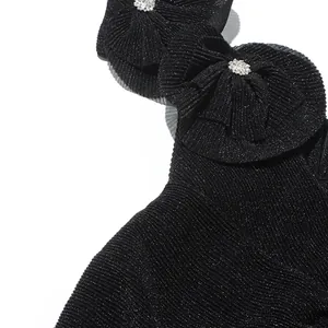 Nahaufnahme eines schwarzen plissierten Kleides mit funkelndem Strassblumen-Detail.