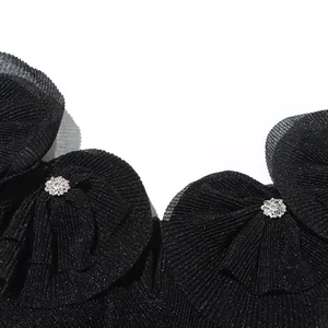 Nahaufnahme von schwarzem Plissee-Stoff mit Schimmer und Strassblumen-Detail am Kleid