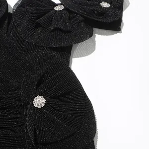 Nahaufnahme des funkelnden schwarzen Faltenstoffs und der Strass-Schleifendetails des Kleides.