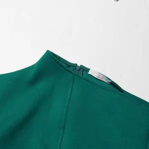 Detailopname van de halslijn van een groene asymmetrische jurk met blinde rits.