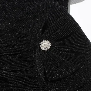 Detailansicht aus schimmerndem schwarzem Plissee-Stoff mit eleganter Kristallbrosche