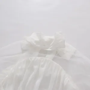 Primer plano de una blusa de gasa blanca con lazo de cinta y detalles de malla fina.