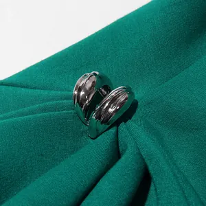 Detailweergave van zilveren metalen gesp op een elegante smaragdgroene geplooide jurk.