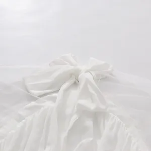 Primer plano de una blusa de gasa blanca con un lazo grande y costuras de malla fina.