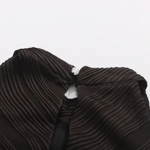 Gros plan sur le bouton raffiné du col arrière d'une robe plissée noire sans manches.