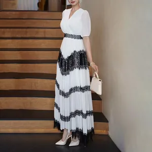 Robe longue blanche élégante à col en V avec dentelle noire et jupe plissée sur escalier
