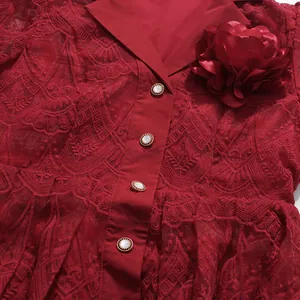 Detailaufnahme eines roten Kleides mit Spitzenstickerei, Perlenknöpfen und Blume